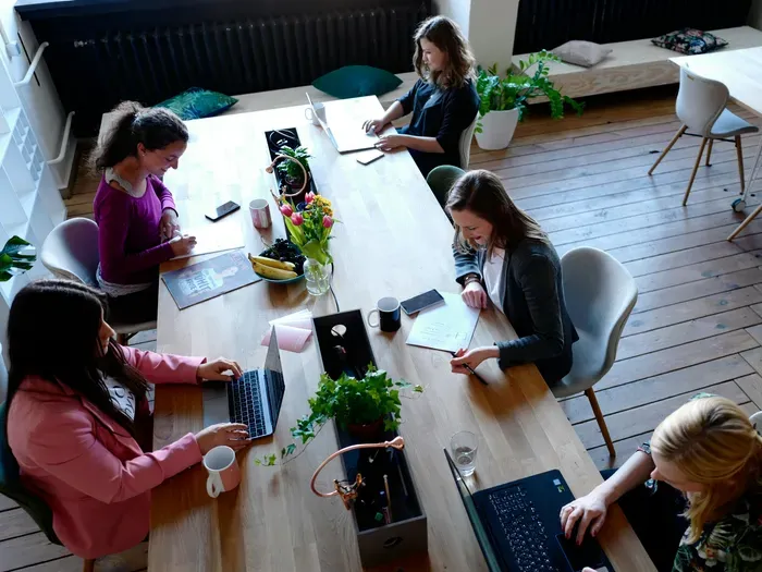 Overhead view of professionals using laptops and notebooks around a wooden table with plants, illustrating a helpful local directory